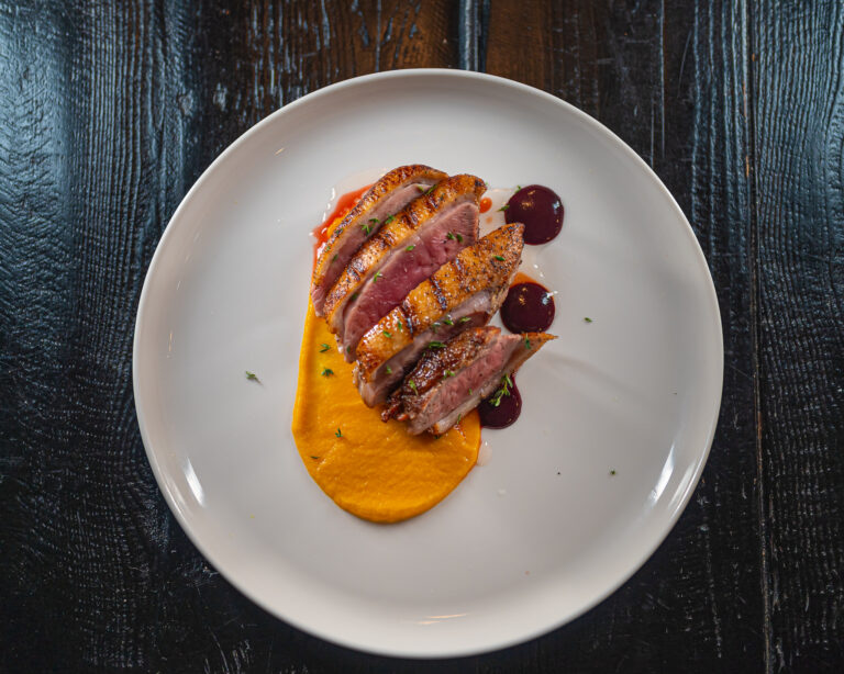 Pan-seared duck breast with cherry sauce, crispy skin sliced over roasted carrot puree with port wine reduction